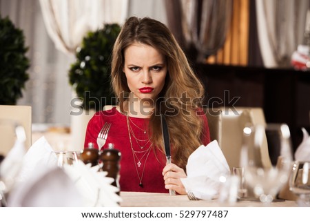 Hungry and angry girl at restaurant with fork and knife, selective focus Royalty-Free Stock Photo #529797487