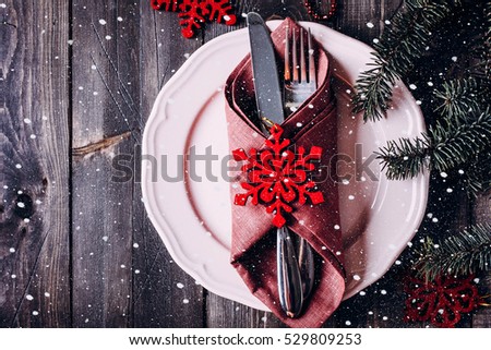 Christmas table setting. Pink plate, knife and fork. Christmas Decorations - red snowflakes, fir branch on wooden background table. Top view