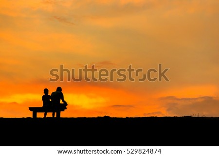 son and dad sitting on Chair at colorful sunset on background