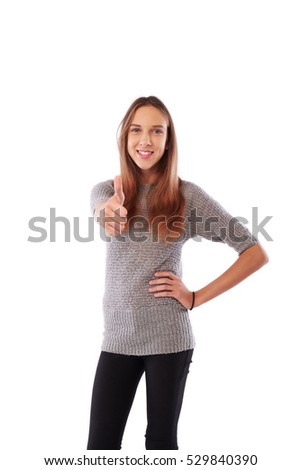Mid shot of skinny happy toothy smiling young girl showing thumb up standing over white background. Holding hand on hip while posing at the camera 