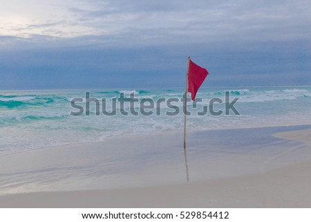 red warning waving flag standing on beach with turquoise water, prohibiting swimming 