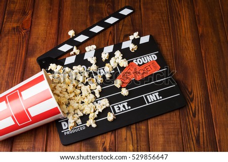 Loose popcorn, striped box, movie tickets and movie clapper on a wooden background
