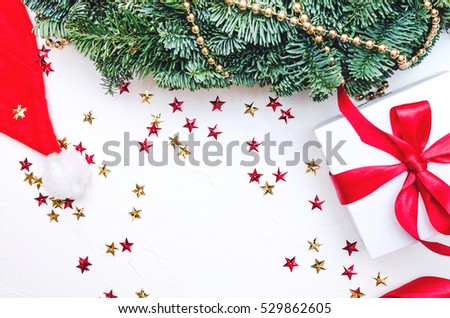 Flat lay, Top view Christmas composition on white background. Natural green pine wreath, gift box with red fabric tape, Santa's cap, spiral ribbon, gold beads, stars confetti. Xmas concept, decor.