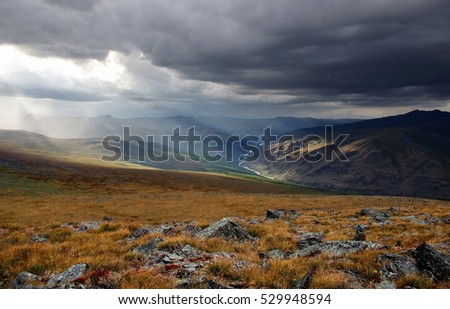 Mountain river valley under a stormy evening dramatic cloudy sky with dark clouds and bright rays of sunset light Plateau Ukok Altai mountains Siberia Russia