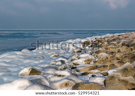 Large stones covered with ice on the Baltic coastline at winter cold sunny day