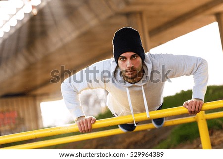 Young man doing push ups on the handrail under the bridge.