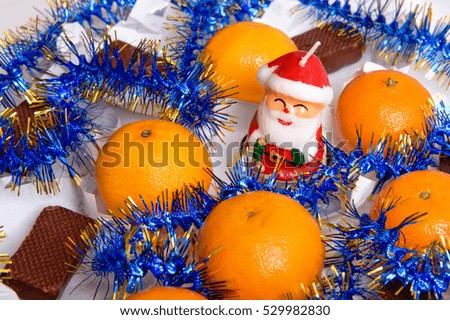 Tangerines, uncovered chocolates, candle Santa Claus and tinsel