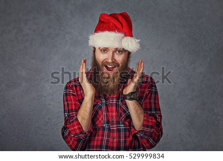Surprised excited happy bearded man wearing red santa claus hat looking shocked by what she saw isolated gray background. Positive emotion
