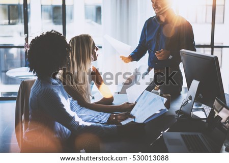 Young team of coworkers making great meeting discussion in modern coworking office.Hispanic businessman talking with two beautiful womans.Teamwork process.Horizontal,blurred background,sun effect