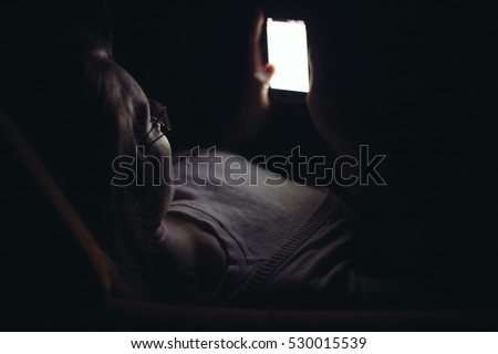 Young woman using mobile phone in dark room at home Royalty-Free Stock Photo #530015539