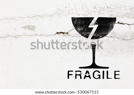An imprint of an icon of a shattered glass and the word fragile on a cracking concrete wall.
