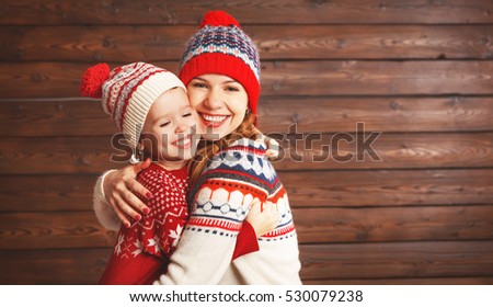 happy family mother and child girl with christmas hat hugs at wooden  background