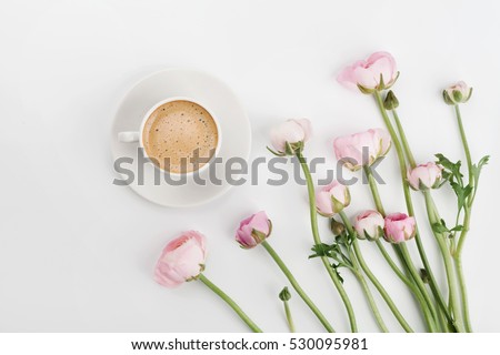 Beautiful spring Ranunculus flowers and cup of coffee on white desk from above. Greeting card. Breakfast. Pastel color. Clean space for text. Flat lay styling
