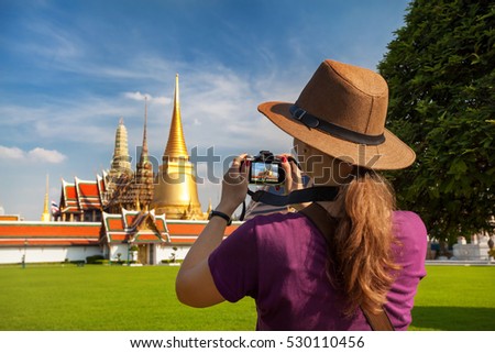Woman tourist in hat taking a picture of Temple of the Emerald Buddha with Golden Stupa in Bangkok 