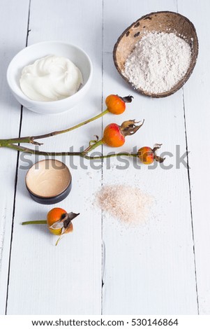 cosmetic cream, clay and bath salt with rose hips on white wood table background