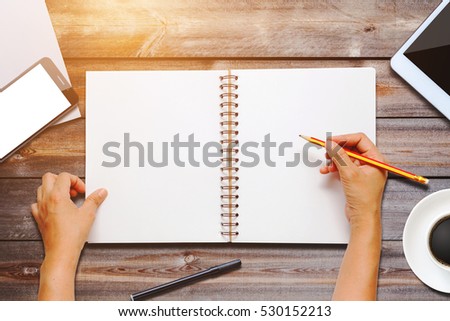 hand holding pencil and writing notebook on a wooden table.