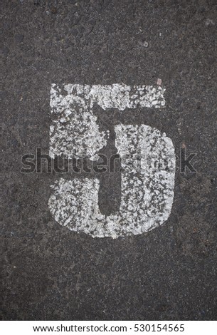 Parking lot number 5. A close up on white stenciled number five on black pavement.