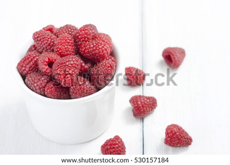 raspberry fruits at white ceramic cup, on bright wood table
