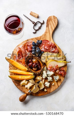Meat and cheese plate antipasti snack with Prosciutto ham, Parmesan, Blue cheese, Cantaloupe melon and Olives on olive wood serving board on concrete background