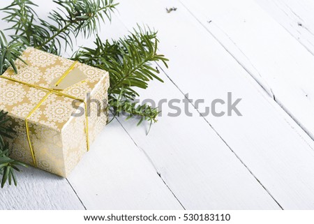 golden gift box and pine branches on white wood background