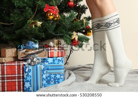 Female feet in socks near Christmas tree with presents.