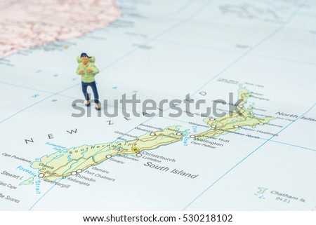 closeup of miniature figurine of young traveler standing on big map next to New Zealand islands