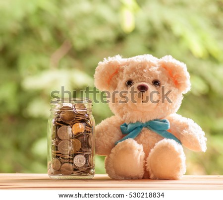 Teddy bear and jar of coins on wooden table with nature background, Money saving concept