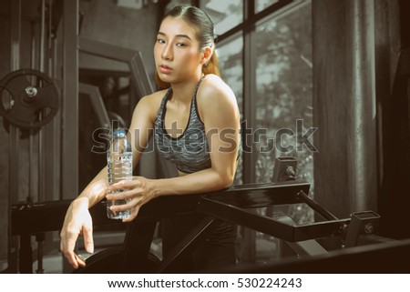 Toned picture,Asian women at gym,Fitness girl training in sport club with exercise equipments. Woman holding bottle of water.