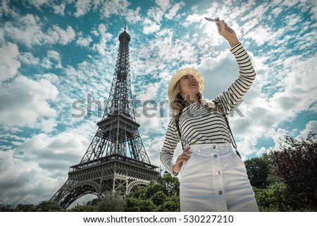 Woman tourist selfie near the Eiffel tower in Paris under sunlight and blue sky. Famous popular touristic place in the world.