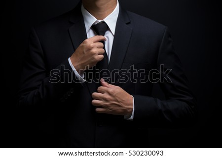 Man in black suit and adjusting his necktie Royalty-Free Stock Photo #530230093