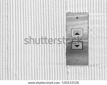 Closeup surface elevator button in up and down arrow sign on cement wall textured background in black and white tone with copy space