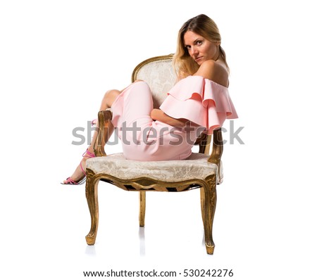 Pretty model woman posing in studio with a pink dress on vintage armchair