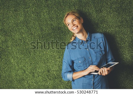 Young woman posing with tablet by green wall