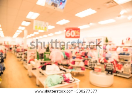 Blurred children clothing store with discount sign and variety of clothes for newborn, kids, toddlers, babies. Colorful shirts, trousers, pants, blouses, bodysuits arranged on shelves and hangers.