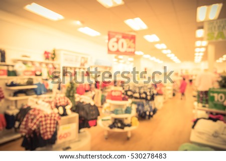Blurred children clothing store with discount sign and variety of clothes for newborn, kids, toddlers, babies. Colorful shirts, trousers, pants, blouses, bodysuits on shelve, hanger. Customer shopping