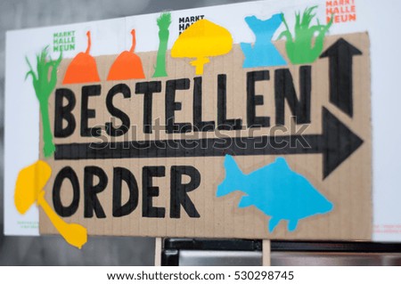 Sign plate in German and English made of cardboard paper, that says "Order". With the pictures of fishes and mushrooms 