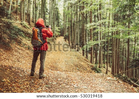 Man hiker standing in autumn mountain forest holding a camera, taking pictures. Hiking and travel concept. Colourful nature background.