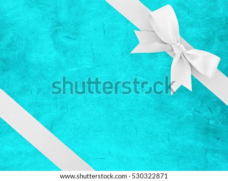 white ribbon bow wrapped around corner of blue paper with abstract striped pattern, simple tied bow and bright blue cardboard for cover gift box decor or greeting card, flat lay close up top view