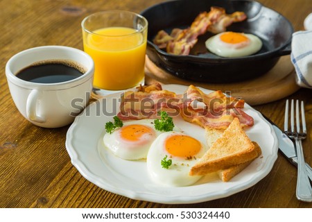 American breakfast with sunny side up eggs, bacon, toast, pancakes, coffee and juice, wood background Royalty-Free Stock Photo #530324440