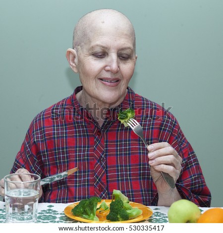 Proper nutrition after chemotherapy. Bald woman at the table eating broccoli, fruit