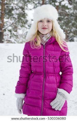 In winter, the snow-covered forest stands blond girl in a pink coat.