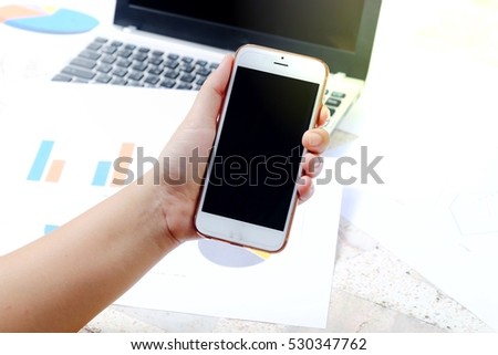 Soft focus Close up working on pc holding smartphone and looking at screen with diagrams. Office person using mobile phone and laptop