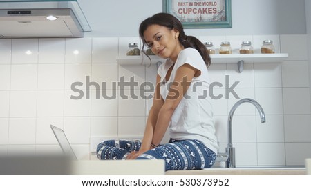 Smiling black woman using computer in modern kitchen interior.
