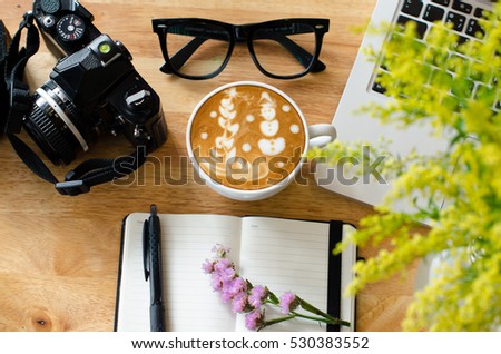 Snowman latte art on wood table with laptop, glass, vintage camera and notebook 