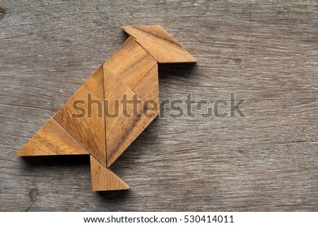 Tangram puzzle as bird shape on old wood background