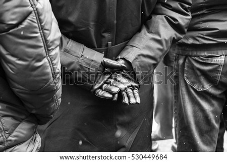 black leather gloves/Military person in a crowd during the national day of Romania wearing an uniform and having his hands crossed in the back wearing black leather gloves.