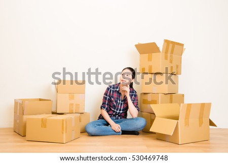 people moving new place and repair concept - happy young woman thinking with many cardboard boxes sitting on floor at home. mixed race asian chinese model