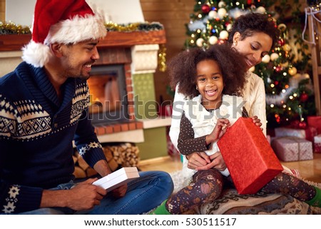 Very nice smiling black girl with parents opening Christmas gifts 