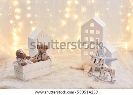 Baby toys and toy house on a background of Christmas lights. Holiday decor, children's room. New year. Bear and a wooden horse