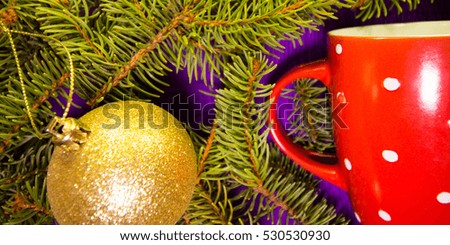 Needles on purple background with golden ball and red Christmas cup with white dots.